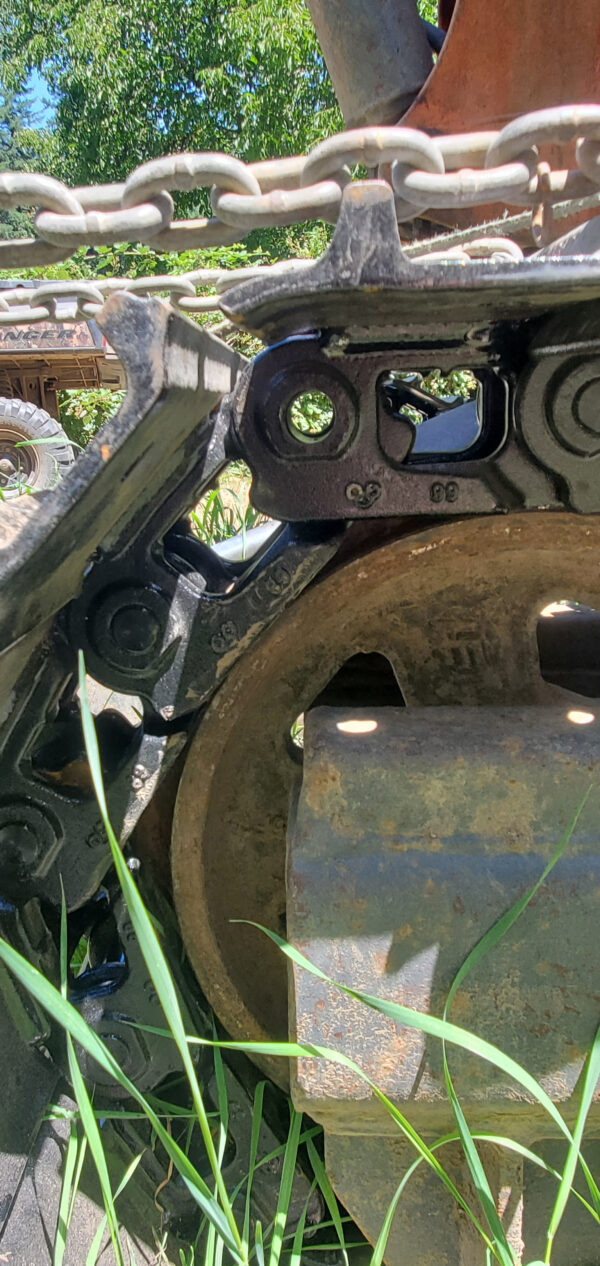 Close-up of Steel tracks Kubota KH90, showing the wheel mechanism with green grass and trees in the background. | VIQAN Replacement Parts for Heavy Equipment - Rubber and Steel Tracks