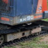A Steel tracks Kubota KH90 excavator, compact and colored orange and blue, is parked on grass near a red tractor and scattered tools. | VIQAN Replacement Parts for Heavy Equipment - Rubber and Steel Tracks