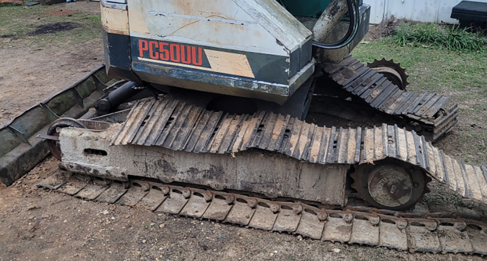 An excavator with broken steel tracks lying on the ground. - Viqan Replacement Tracks & Undercarriage Parts for Heavy Equipment