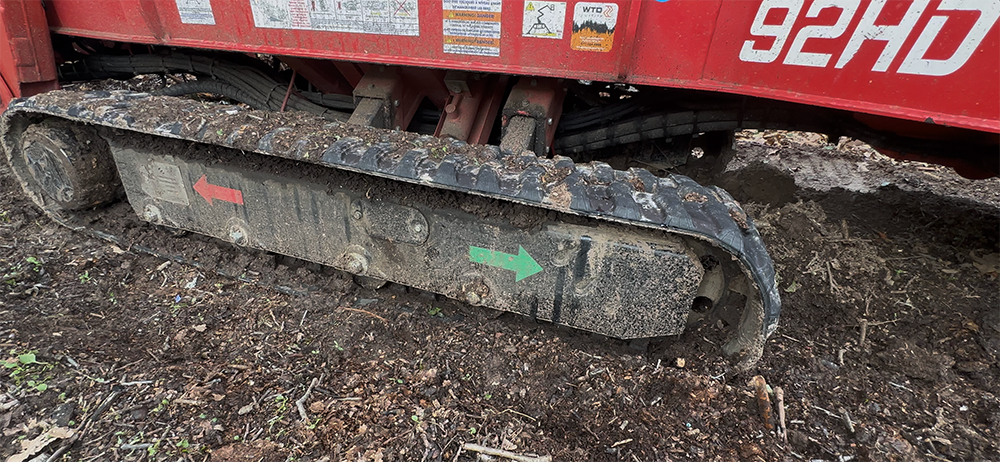 Close-up of the muddy tracks of a 92HD+ Arbor Pro parked on soil. Two arrows, one red and one green, are painted on the side of the tracks. | VIQAN Replacement Parts for Heavy Equipment - Rubber and Steel Tracks